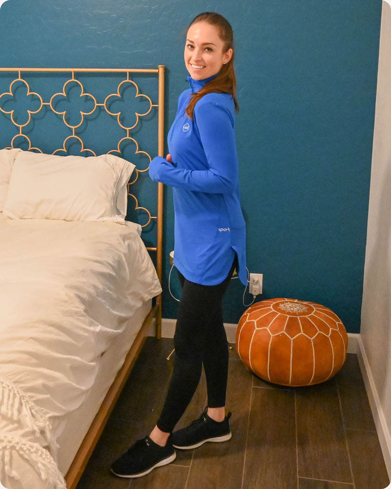 A customer smiling and posing while wearing a royal blue Spark Half-Zip, a modest activewear sweatshirt from Veil Garments.