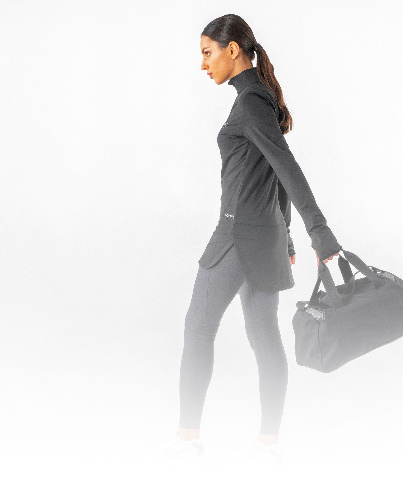 A female holding a gym bag while wearing a black Spark Half-Zip, a modest activewear sweatshirt from Veil Garments.