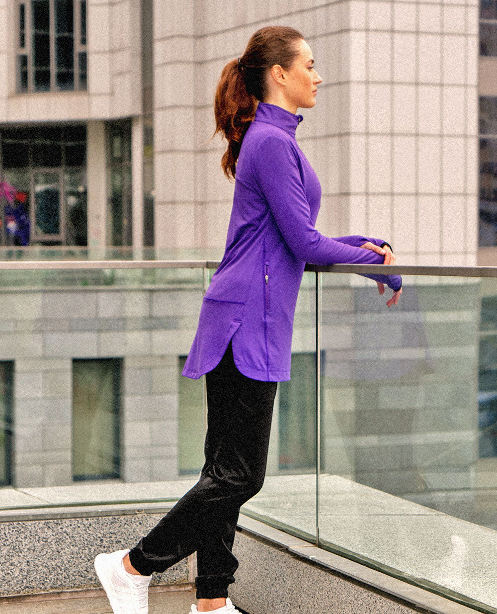 A female wearing a purple Spark Half-Zip, a Veil Garments modest activewear product, in an outdoor setting.