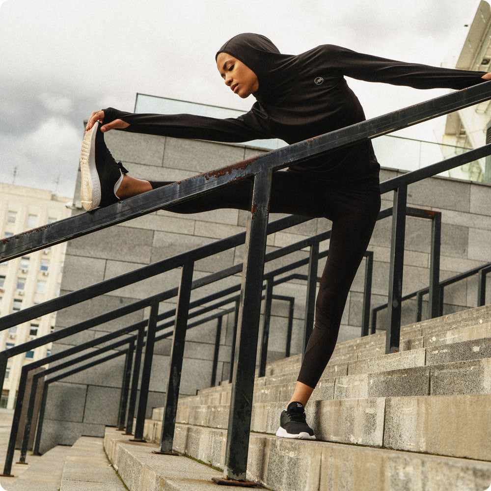 A female exercising outdoor in a black Halo Running Hoodie, a modest activewear sweatshirt from Veil Garments.