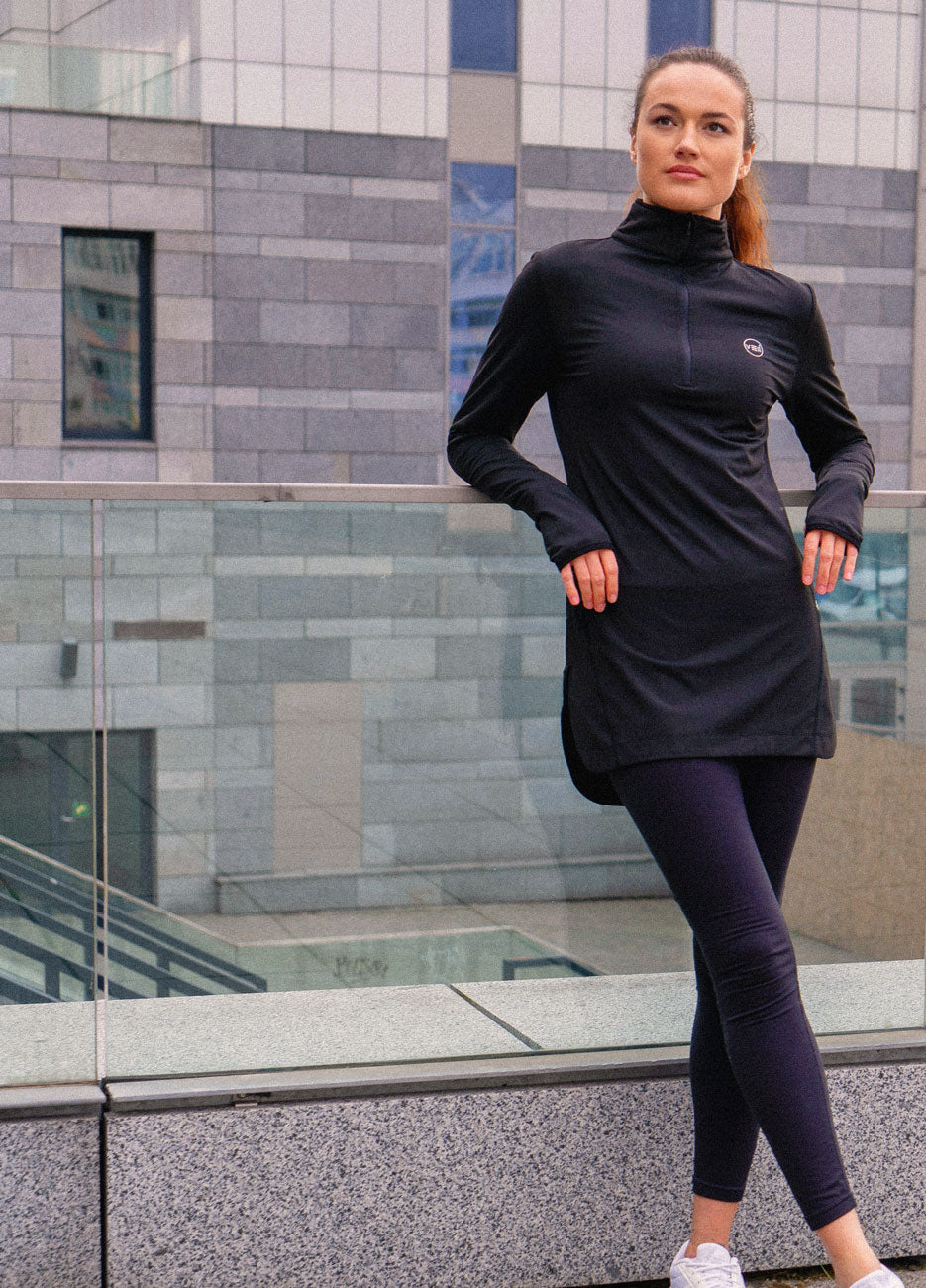 A female wearing a Veil Garments Black Spark Half-Zip, modest activewear, in an outdoor setting.
