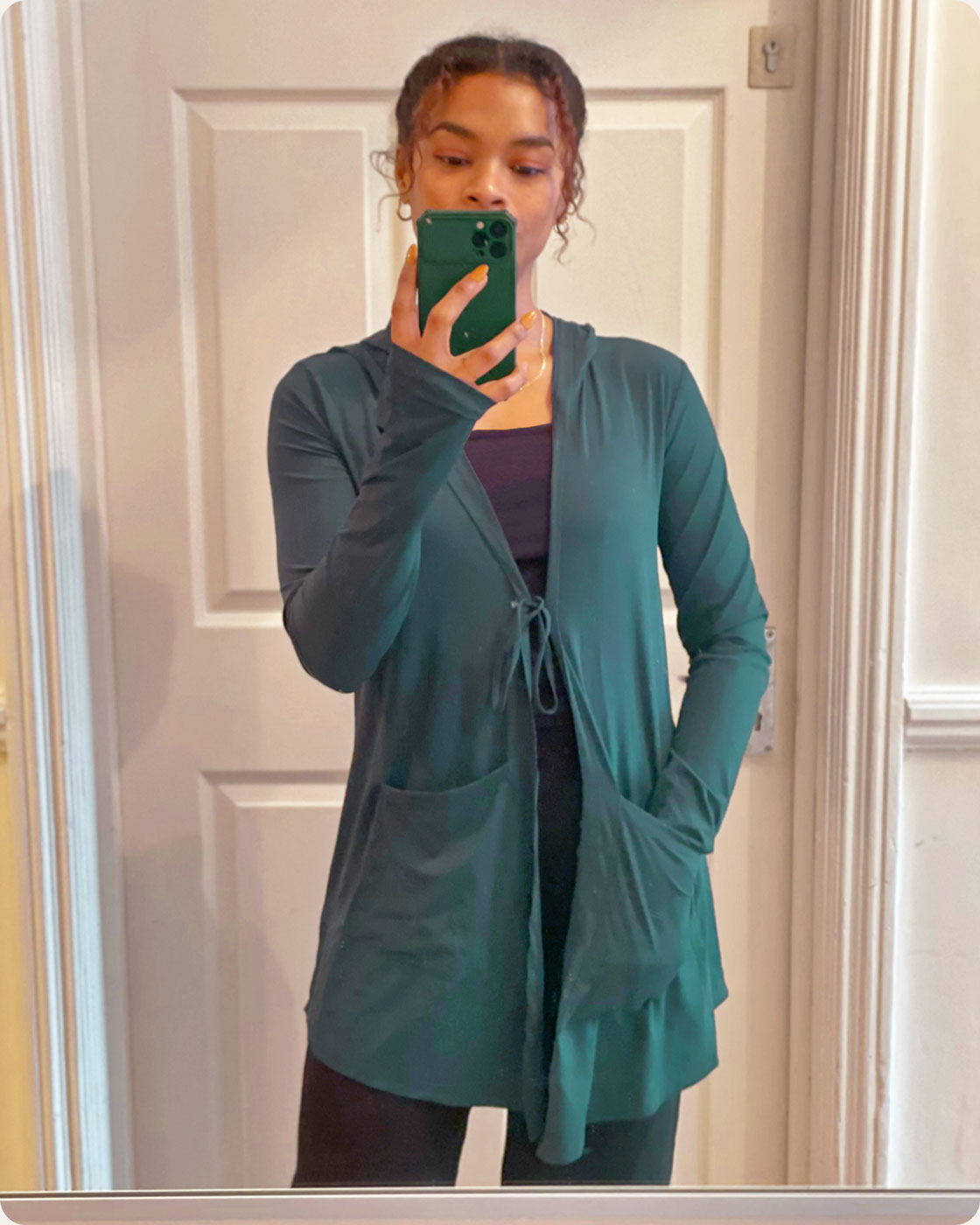 A customer taking a selfie while posing in an emerald green Move It Cardigan, a modest sportswear cardigan from Veil Garments.