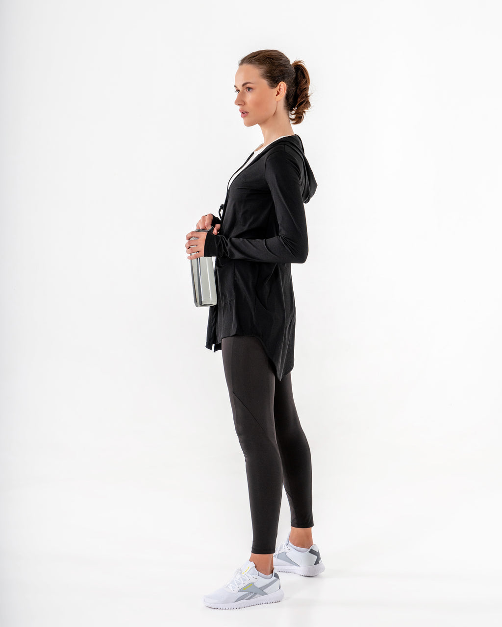 Black Move It Cardigan seen in profile, hood down, worn with leggings and a water bottle in hand.

#color_black