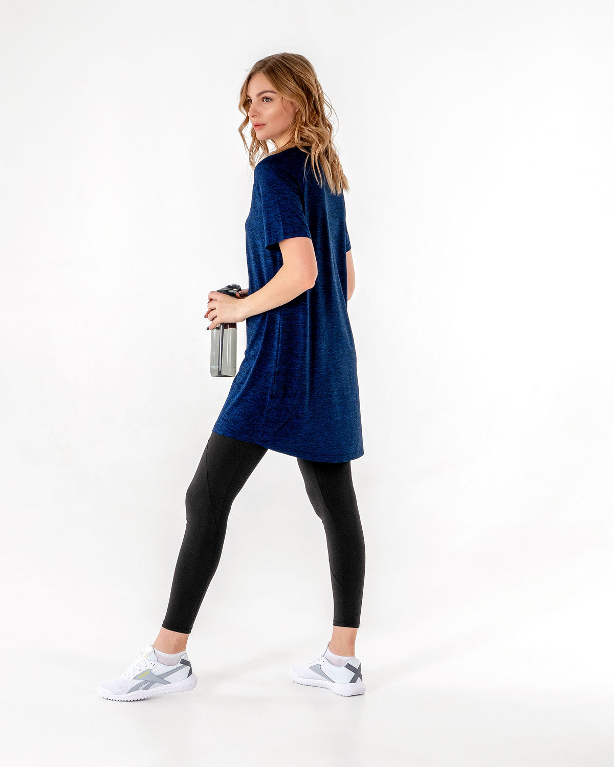 Full-length back view of the Connect T-Shirt Dress in Blue/Black, worn walking with a water bottle in hand.

#color_blue-black
